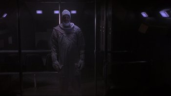 Movie still from “Phantoms” (1998), directed by Joe Chappelle – A man in a black suit standing in a dark room; Wide shot, Low angle