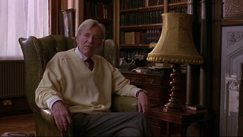 Movie still from “Phantoms” (1998), directed by Joe Chappelle – An older man sitting in a chair next to a lamp; Medium shot, Over the shoulder angle