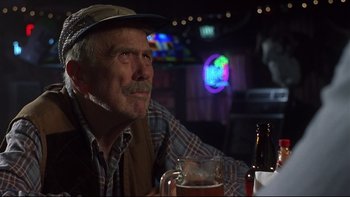 Movie still from “Phantoms” (1998), directed by Joe Chappelle – An older man sitting at a table with a glass of beer in front of him; Close Up shot, Low angle