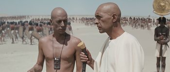 Two bald men standing next to each other on the beach