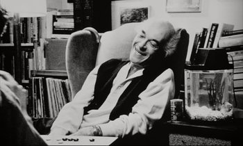 Movie still from “Pi” (1998), directed by Darren Aronofsky – An older man sitting in a chair smiling; Medium shot, Low angle