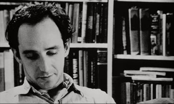 Movie still from “Pi” (1998), directed by Darren Aronofsky – Black and white photograph of a man in front of bookshelves; Close Up shot, High angle