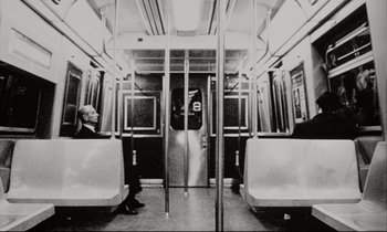 Movie still from “Pi” (1998), directed by Darren Aronofsky – A black and white photo of two people sitting on a subway train; Wide shot, Low angle
