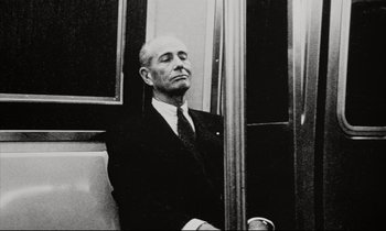 Movie still from “Pi” (1998), directed by Darren Aronofsky – An older man in a suit and tie sitting on a train; Medium shot, Low angle