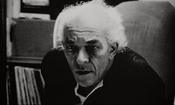 Movie still from “Pi” (1998), directed by Darren Aronofsky – An older man with white hair is looking at the camera; Close Up shot, Low angle