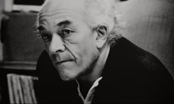 Movie still from “Pi” (1998), directed by Darren Aronofsky – An older man with white curly hair wearing a black shirt; Close Up shot, Low angle