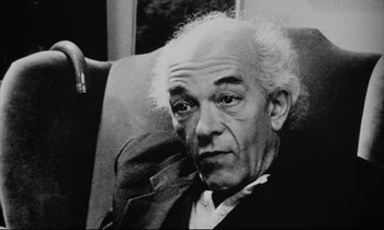 Movie still from “Pi” (1998), directed by Darren Aronofsky – An older man sitting in a chair looking at the camera; Close Up shot, Low angle