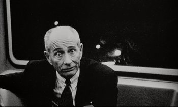 Movie still from “Pi” (1998), directed by Darren Aronofsky – An older man wearing a suit and tie sitting in a car; Close Up shot, Low angle