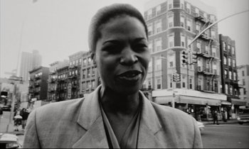 Movie still from “Pi” (1998), directed by Darren Aronofsky – A black and white photo of a woman in front of buildings; Close Up shot, Low angle
