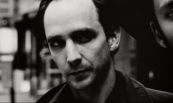 Movie still from “Pi” (1998), directed by Darren Aronofsky – Black and white photograph of a man in a black shirt; Close Up shot, Low angle