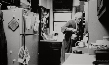 Movie still from “Pi” (1998), directed by Darren Aronofsky – An older man in a robe is pouring a cup of coffee; Medium shot, Low angle