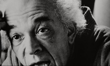 Movie still from “Pi” (1998), directed by Darren Aronofsky – An older man with a white beard is smiling for the camera; Close Up shot, Low angle