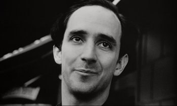 Movie still from “Pi” (1998), directed by Darren Aronofsky – Black and white photograph of a man with a smirk on his face; Close Up shot, Low angle