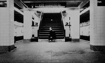 Movie still from “Pi” (1998), directed by Darren Aronofsky – A man sitting on the ground in front of a staircase; Wide shot, Low angle