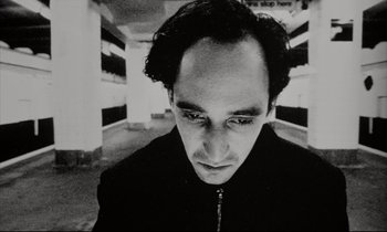 Movie still from “Pi” (1998), directed by Darren Aronofsky – Black and white photograph of a man in a black jacket; Close Up shot, Low angle