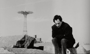Movie still from “Pi” (1998), directed by Darren Aronofsky – A black and white photo of a man sitting on a rock; Medium shot, Low angle