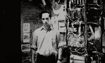 Movie still from “Pi” (1998), directed by Darren Aronofsky – A black and white photo of a man standing in a room; Medium shot, Low angle