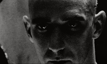 Movie still from “Pi” (1998), directed by Darren Aronofsky – A man's face with eyes looking into the camera; Extreme Close Up shot, Low angle