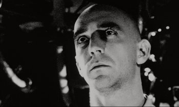 Movie still from “Pi” (1998), directed by Darren Aronofsky – Black and white photograph of a man looking into the distance; Close Up shot, Low angle