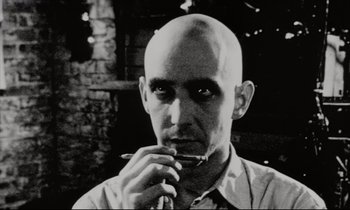 Movie still from “Pi” (1998), directed by Darren Aronofsky – A man with a bald head is smoking a cigarette; Close Up shot, Low angle