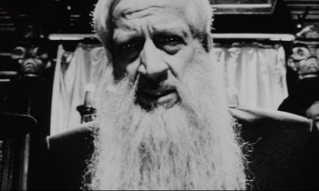 Movie still from “Pi” (1998), directed by Darren Aronofsky – An old man with a long beard and a white hat; Close Up shot, Low angle