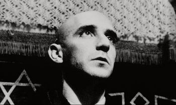 Movie still from “Pi” (1998), directed by Darren Aronofsky – An old black and white photo of a man with a bald head; Close Up shot, Low angle