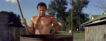 Movie still from “Picnic” (1955), directed by Joshua Logan – A shirtless man standing in front of an oil tank; Medium shot, Low angle