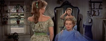 Movie still from “Picnic” (1955), directed by Joshua Logan – A woman is looking in the mirror in front of a mirror; Medium shot, Over the shoulder angle