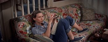 Movie still from “Picnic” (1955), directed by Joshua Logan – A woman sitting on a couch holding a book; Medium shot, High angle
