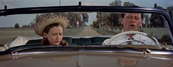 Movie still from “Picnic” (1955), directed by Joshua Logan – A woman in a cowboy hat in the back seat of a car; Close Up shot, Over the shoulder angle