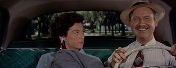 Movie still from “Picnic” (1955), directed by Joshua Logan – A woman sitting in the back seat of a car while holding a steering wheel; Close Up shot, Over the shoulder angle