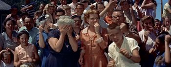 Movie still from “Picnic” (1955), directed by Joshua Logan – A group of people standing around each other in front of a crowd; Medium shot, High angle