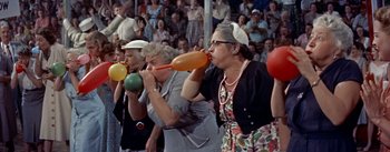 Movie still from “Picnic” (1955), directed by Joshua Logan – A group of women drinking from balloons in front of an audience; Medium shot, High angle