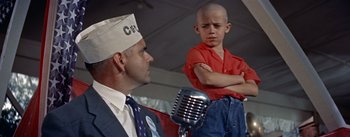 Movie still from “Picnic” (1955), directed by Joshua Logan – An older man and a young boy are sitting in front of a microphone; Medium shot, Low angle