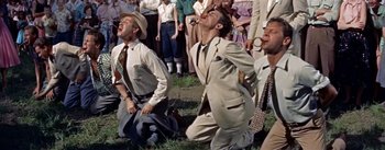 Movie still from “Picnic” (1955), directed by Joshua Logan – A group of men in suits and ties are standing in the grass; Medium shot, Low angle