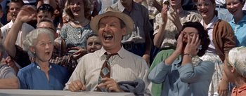 Movie still from “Picnic” (1955), directed by Joshua Logan – A man in a hat and tie laughing in front of a group of people; Medium shot, Low angle