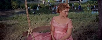 Movie still from “Picnic” (1955), directed by Joshua Logan – A woman in a pink dress sitting on a bench; Medium shot, High angle