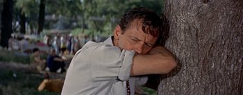 Movie still from “Picnic” (1955), directed by Joshua Logan – A man leaning against a tree with his head resting on the arm of the tree; Close Up shot, Low angle