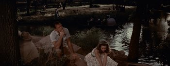Movie still from “Picnic” (1955), directed by Joshua Logan – A man and a woman sitting next to a body of water; Medium shot, High angle