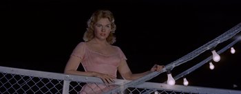 Movie still from “Picnic” (1955), directed by Joshua Logan – A woman in a pink dress leaning on a fence; Medium shot, Low angle