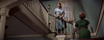 Movie still from “Picnic” (1955), directed by Joshua Logan – A woman in a blue shirt is standing at the top of a staircase; Wide shot, Low angle