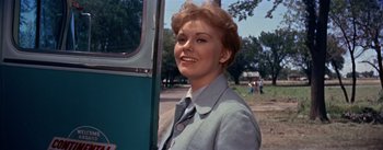 Movie still from “Picnic” (1955), directed by Joshua Logan – A woman standing next to a bus on the side of the road; Close Up shot, Low angle