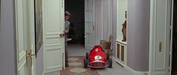 Movie still from “Pierrot le Fou” (1965), directed by Jean-Luc Godard – A man standing next to a red toy race car; Wide shot, Over the shoulder angle