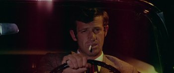 Movie still from “Pierrot le Fou” (1965), directed by Jean-Luc Godard – A man sitting in the drivers seat of a car while smoking a cigarette; Close Up shot, Low angle