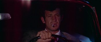 Movie still from “Pierrot le Fou” (1965), directed by Jean-Luc Godard – A man in a suit smoking a cigarette while holding a cane; Close Up shot, Low angle
