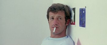 Movie still from “Pierrot le Fou” (1965), directed by Jean-Luc Godard – A man smoking a cigarette while leaning against a wall; Close Up shot, Low angle