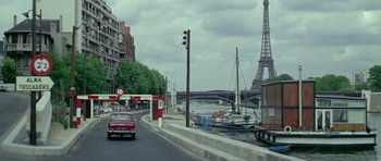 Movie still from “Pierrot le Fou” (1965), directed by Jean-Luc Godard – A car driving down a street next to a river; Extreme Wide shot, High angle
