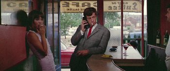 Movie still from “Pierrot le Fou” (1965), directed by Jean-Luc Godard – A man in a suit and tie talking on a phone; Medium shot, Low angle