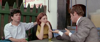 Movie still from “Pierrot le Fou” (1965), directed by Jean-Luc Godard – A woman sitting at a table talking to two other people; Medium shot, Over the shoulder angle