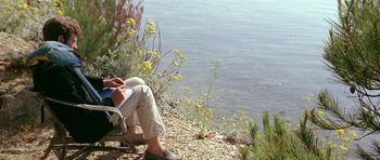 Movie still from “Pierrot le Fou” (1965), directed by Jean-Luc Godard – A person sitting on a bench next to a body of water; Wide shot, High angle